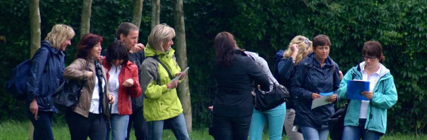 Gruppe erkundet mit Karten und Tablets ein Gelände im Grünen – Educaching in der Praxis